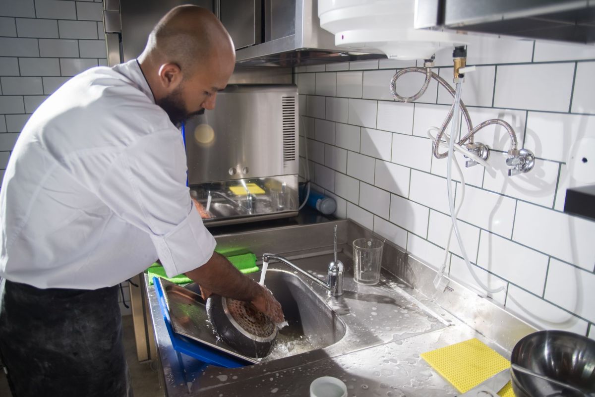 Cook washing equipment at a stainless sink in a commercial kitchen