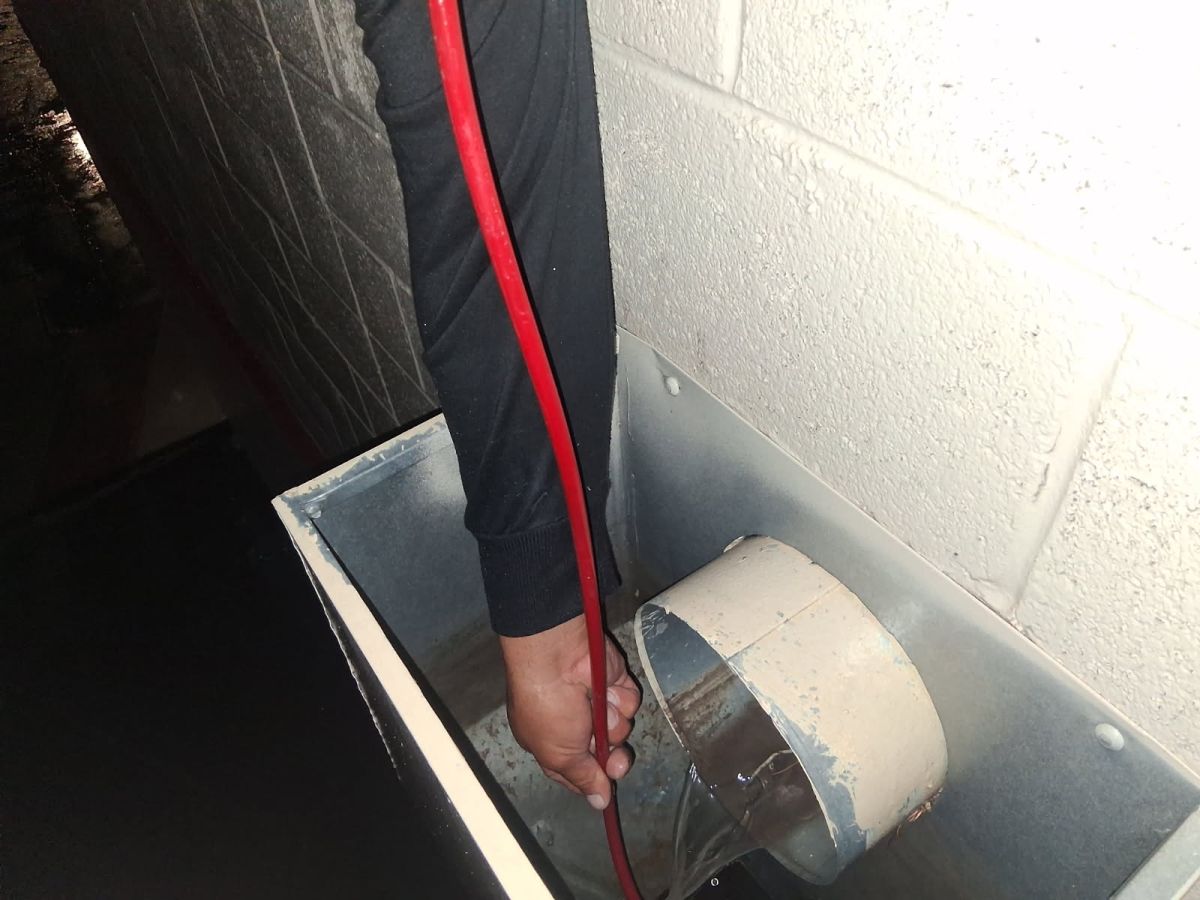 Technician feeding a drain cable into a roof scupper box
